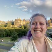 white woman in her 30's with purple and blonde hair standing in front of edinburgh castle on a sunny day