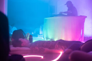 People lying on the floor, a man behind a large table djing.