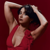 a woman with dark hair in a red dress holding up arms up and a darker red background.